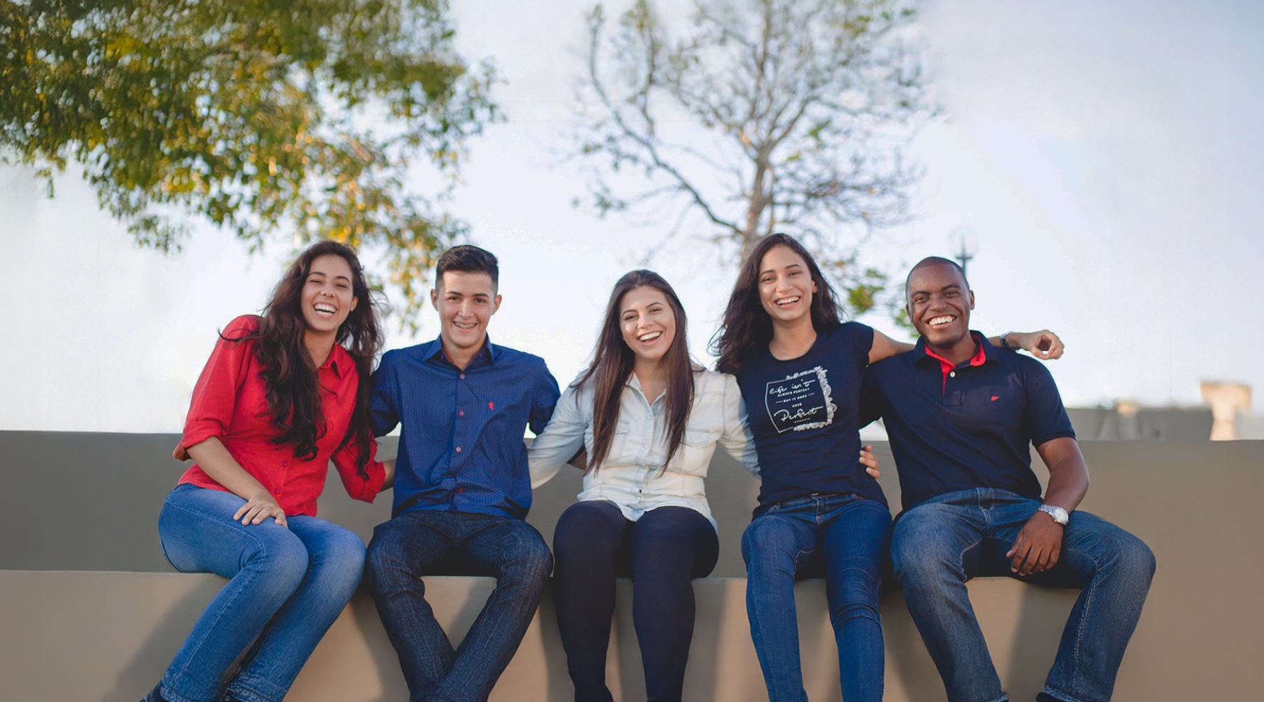 college residents sit on a bench with arms around each other and smile at the camera