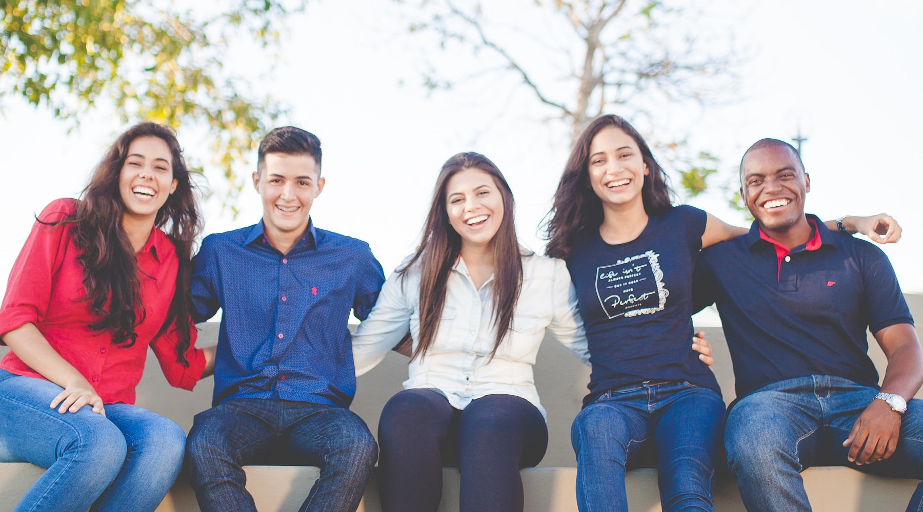 Be Part of a Legacy college residents sit on a bench with arms around each other and smile at the camera